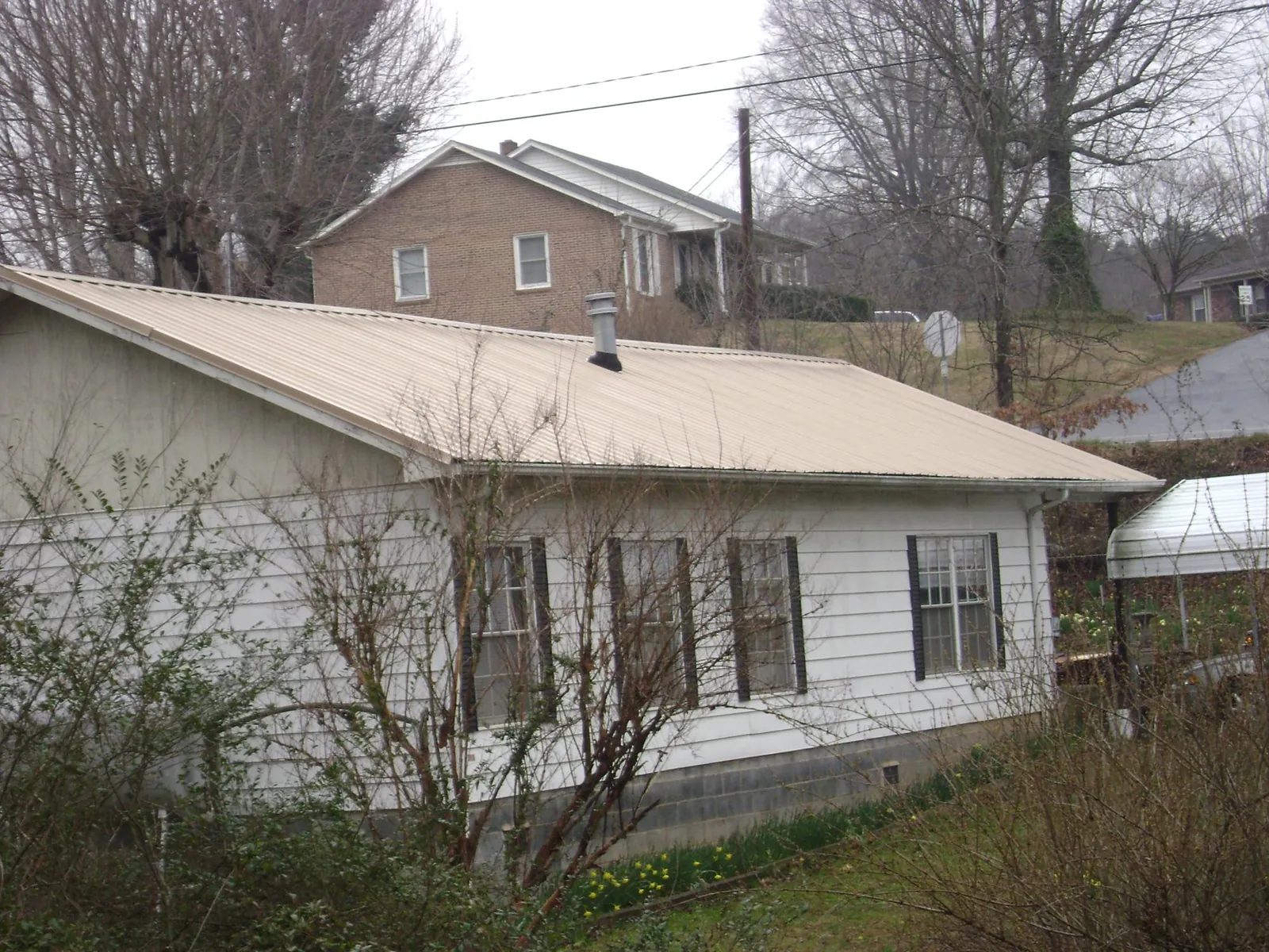 Tan metal roof on a white sided house set into a hillside in Oxford